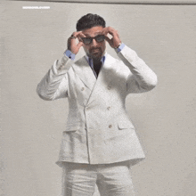 a man in a white suit and blue shirt is standing in front of a wall .