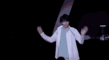 a young man in a white jacket and a blue shirt is dancing on a stage .