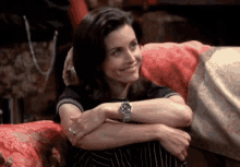 a woman wearing a watch sits on a couch with her arms crossed