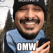 a man with a beard and a nose ring is smiling and holding a cell phone with the word omw above his head