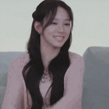 a woman in a pink sweater is sitting on a couch smiling .