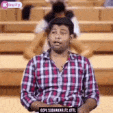 a man in a plaid shirt is sitting in a lecture hall talking .