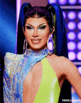 a woman with blue hair and hoop earrings is wearing a yellow and blue dress .
