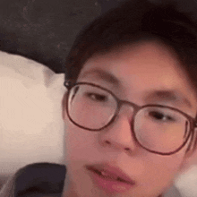 a young boy wearing glasses is laying on a bed .