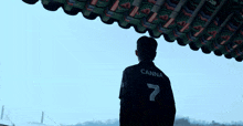 a man wearing a canna 7 jersey stands under a roof