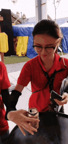 a woman in a red shirt holds a can of beer