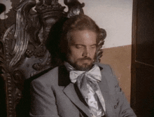 a man in a suit and bow tie is sitting in a chair with his eyes closed
