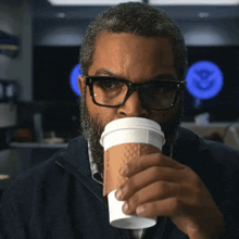 a man wearing glasses is drinking from a cup that says ' ice cube ' on it