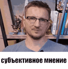 a man wearing glasses and a blue shirt is standing in front of a book shelf .