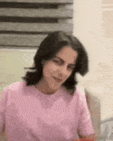 a woman in a pink t-shirt is sitting on a couch and making a funny face .
