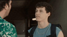 a man with curly hair is wearing a blue tank top and a gold chain necklace