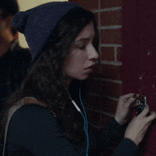 a woman wearing a beanie and ear buds is holding a cell phone