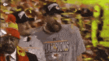 a man wearing a champions t-shirt is standing next to another man in a crowd .