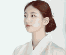 a close up of a woman wearing a white kimono with her hair in a bun