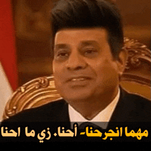 a man in a suit and tie is sitting in a chair with arabic writing behind him