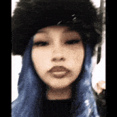 a woman with blue hair is wearing a black hat and looking at the camera .