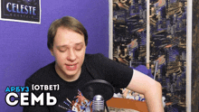 a man stands in front of a microphone with a celeste mountain poster behind him