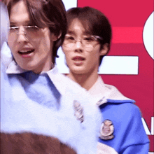 two young men wearing glasses are standing next to each other in front of a red background .