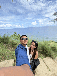 a man and a woman are posing for a picture in front of the ocean