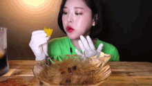 a woman in a green shirt and white gloves is eating food from a glass bowl