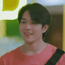 a young man wearing a pink shirt is smiling and looking at the camera