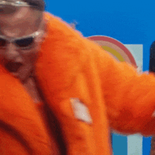 a man wearing an orange coat and sunglasses is dancing