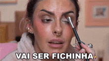 a woman applying makeup with the words vai ser fichinha written above her