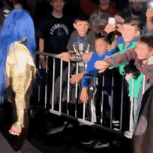 a woman in a blue wig is standing in front of a crowd behind a fence .