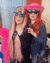 two women are posing for a picture while wearing pink wigs , sunglasses and hats .