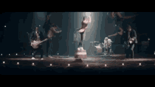a man is dancing on a stage in front of a drum set while a band plays behind him .