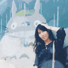 a woman stands in front of a painting of a totoro holding an umbrella