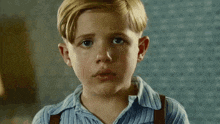 a young boy wearing suspenders and a blue shirt looks at the camera