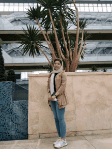 a woman in a hijab stands in front of a tree