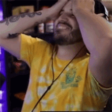 a man with a beard wearing a yellow tie dye shirt is holding his head .