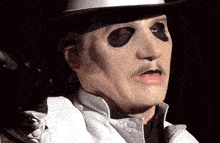 a man with a mask on his face is wearing a cowboy hat and a white jacket .