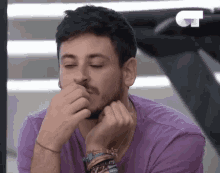 a man in a purple shirt is covering his face with his hands