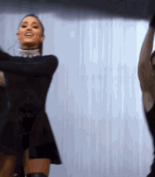 ariana grande is wearing a black dress and knee high boots while dancing on a stage .