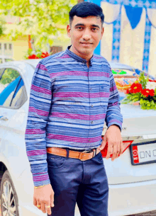 a man in a striped shirt stands in front of a white car with a license plate that says on c