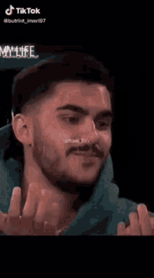 a man with a beard is smiling with his fist in the air while wearing a green hoodie .