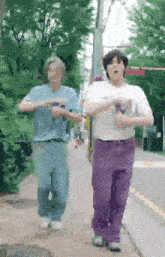 two men are walking down a sidewalk holding hands and making funny faces .