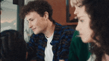 a man in a plaid shirt is looking at something while a woman looks on