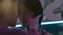 a person touches another person 's face in front of a sign that says ' a ' on it