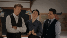 two men and a woman are standing in front of a blackboard with a house on it