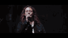 a woman singing into a microphone in front of a large screen that says ' a ' on it
