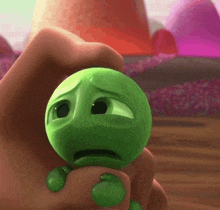 a person is holding a small green cartoon character with a sad face