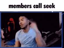 a man in a blue shirt is sitting in front of a computer screen with the words members call seek above him .