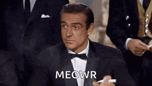 a man in a tuxedo and bow tie is holding a cigarette in his hand .