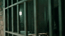 a prison cell with a bed and a lamp in the background behind bars .