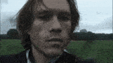 a close up of a man 's face in a field with trees in the background