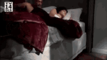 a man and a woman are sleeping in a bed with a tv 14 dls logo in the background